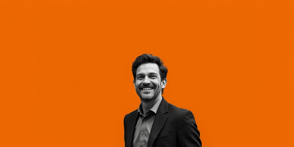 a man is smiling while standing in front of an orange background with a black and white photo of him