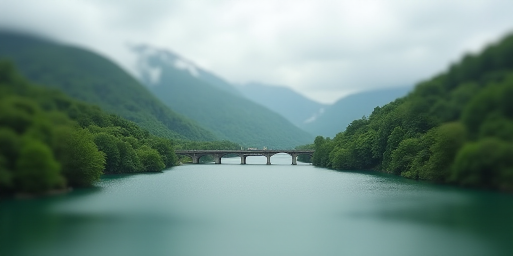 a large body of water surrounded by lush green hills and trees on a cloudy day with a bridge in the