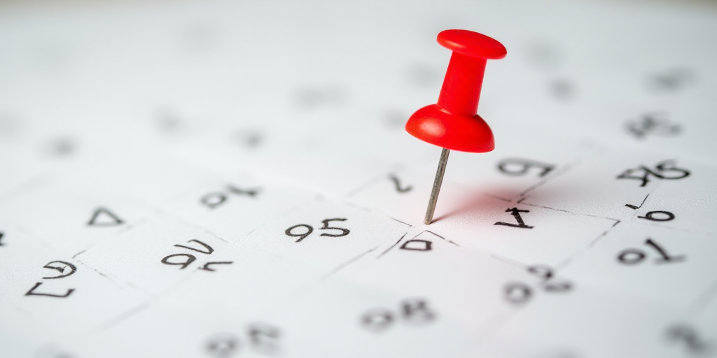 a red pin on a calendar with numbers and date marks on it, with a red pin stuck in the middle of the