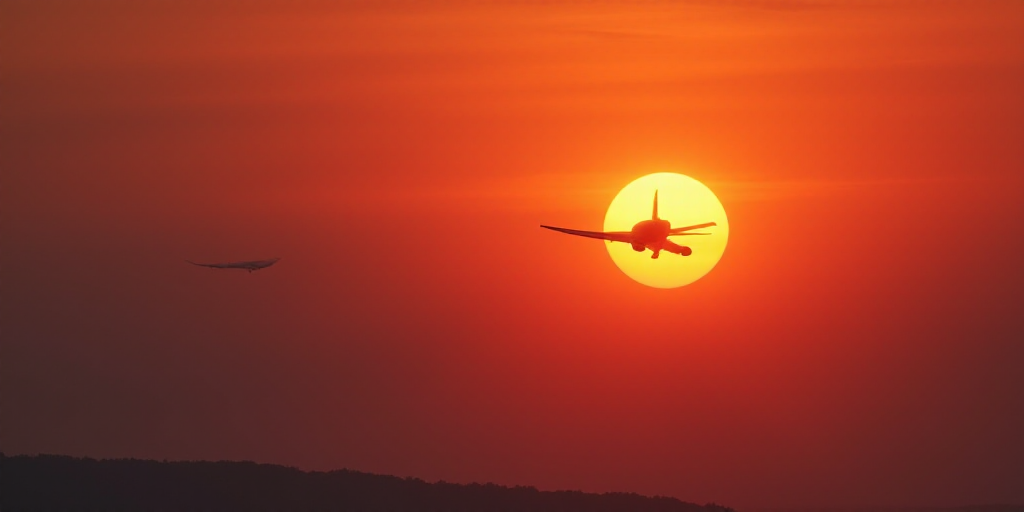 a plane flying in the sky with the sun in the background and a red sky behind it with a plane in the