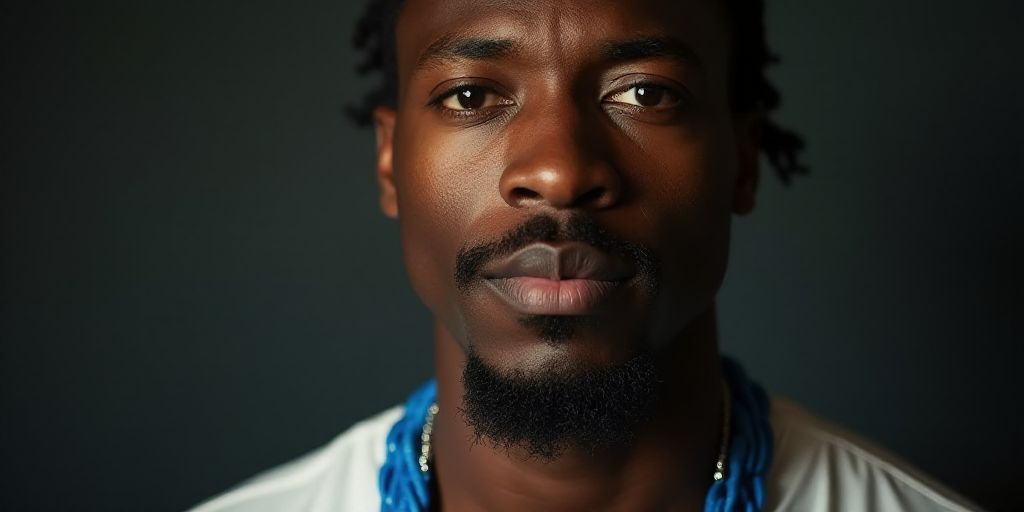 a man with a blue necklace on his neck looking at the camera with a serious look on his face, A. B.