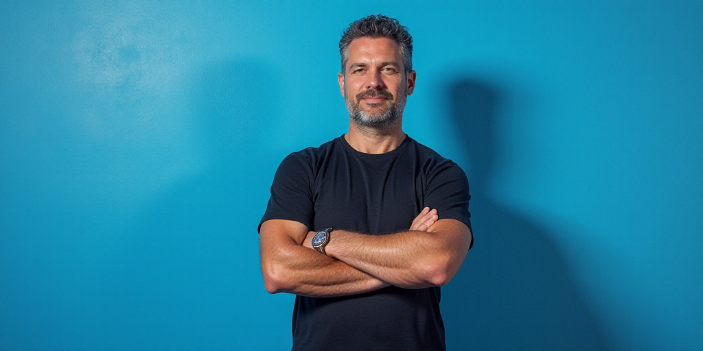 a man with his arms crossed standing in front of a blue background with a black and white photo of h